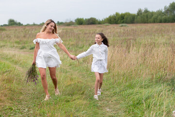 Mother and daughter enjoy a summer stroll through a lush green field, holding hands and picking flowers together while smiling warmly