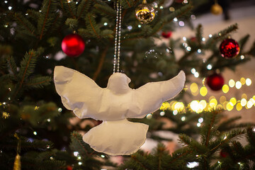 White dove decoration hangs on a Christmas tree adorned with colorful ornaments and warm lights
