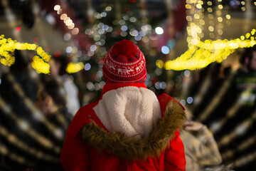 Person in red coat and festive hat enjoys a holiday festival filled with lights and decorations on a winter evening