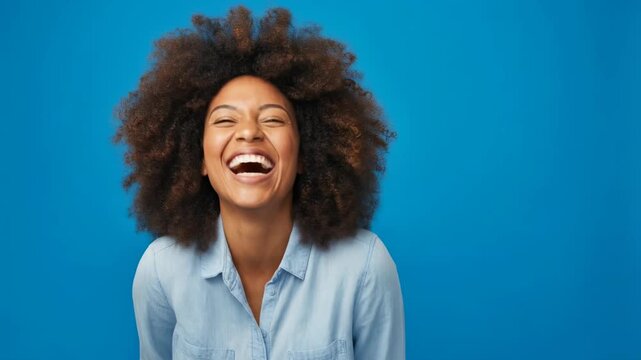 Joyful young woman laughing against a bright blue background, showcasing happiness and positivity