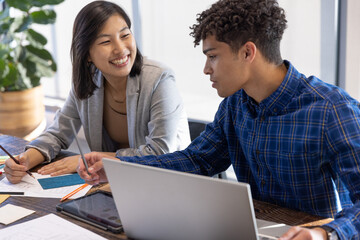 Obraz premium Diverse coworkers reviewing printed sketches, fabric sample at office table with laptop tablet