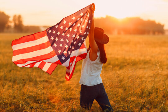 Patriotic Independence day 4th of July Woman farmer in agricultural wheat field with american flag on sunset.