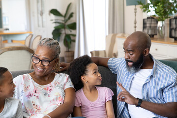 Obraz premium African American family sitting on dark upholstered sofa with throw pillows in living room