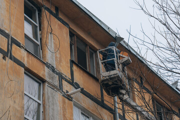 A utility worker uses a boom lift to carry out repairs on the upper floors of a damaged residential building. Infrastructure and glazing are being restored following shelling in the conflict zone.