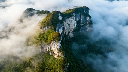 Aerial view of a mist-covered mountain peak surrounded by clouds and dense forest
