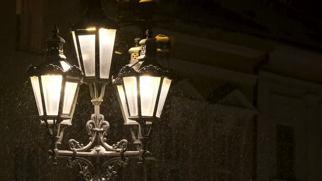 Classic European street lamp in an old town at night during winter. Snowflakes shimmer in the warm light. Lamp positioned on the left side, cinematic background for titles.