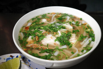 closeup of authentic banh canh ca loc noodle soup with snakehead fish fillets. hue style traditional vietnamese thick rice noodle bowl. hot savory comfort food breakfast with herbs.
