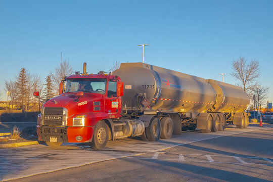 Calgary, Alberta, Canada. January 18, 2026. A red Mack semi-truck pulling double fuel tanker trailers parked in a sunny lot during the golden hour.