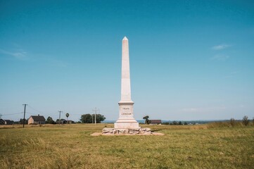 Obraz premium Countryside monument standing alone in grassland with clear sky and rural buildings