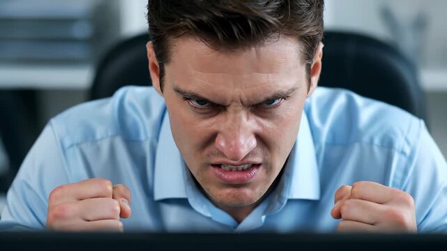 Frustrated businessman showing anger at computer screen. Office environment captures intense emotion. Stress impacts productivity and focus in workplace.