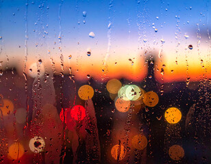 Urban evening glow seen through wet glass with abstract street lights bokeh