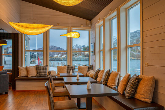Cozy hotel in Hamn, Norway, during winter, offering warm interiors and stunning views of fjords and snow-covered mountains right outside the windows