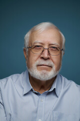 Obraz premium Older man with glasses and white beard looks at the camera against a blue background during an indoor setting