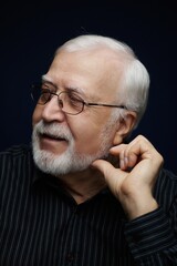 Obraz premium Man with glasses smiles while touching his beard in a dark setting during indoor time