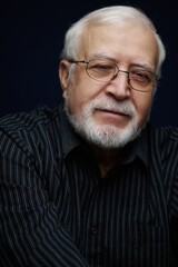 Obraz premium Elderly man with glasses poses for a portrait with a gentle smile in a studio setting