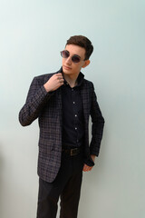 Fototapeta premium Young man poses in stylish outfit with sunglasses against plain background indoors during the day