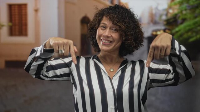 Woman pointing fingers downward on a sunlit cobblestone street outside a building entrance; empowerment.