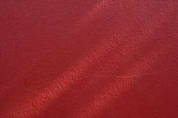 Fototapeta premium Red background painted wall texture with natural light and shadow,showing rough surface detail.Ideal for backgrounds, design material,architectural elements,or construction and interior design project