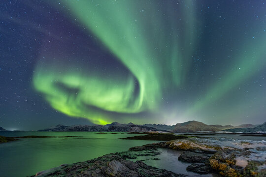 An breathtaking view of Northen Lights over the mountains and sea in Norway