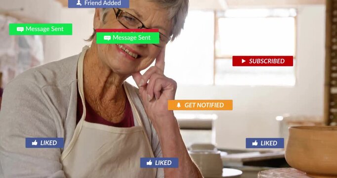 Senior woman wearing apron smiling in pottery shop with floating social media alert icons