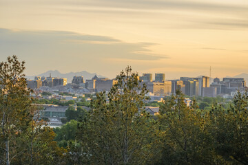 Obraz premium City skyline at sunset viewed from a forested hilltop with distant mountains in the background