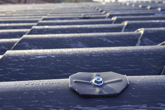 Roofing sandwich panels. Installation of insulated metal sandwich panels. Top view of anthracite-gray metal roofing panels with a tile texture. Bolts with EPDM washers.