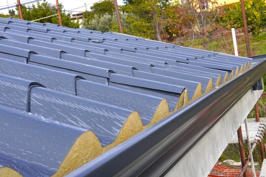 Roofing sandwich panels. Installation of insulated metal sandwich panels. Top view of anthracite-gray metal roofing panels with a tile texture. Bolts with EPDM washers.