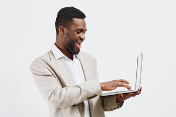 Smiling man wearing beige blazer and white shirt holding a laptop computer, looking at screen with...