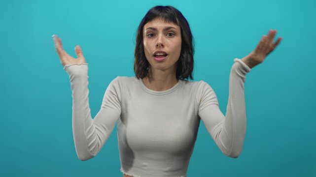 Young hispanic woman rubs eyes in studio while pressing fists to eye sockets against a turquoise wall; astonishment.