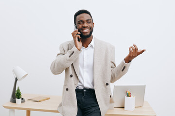 Confident smiling African American man in beige blazer talking on mobile phone while standing at...