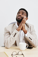 Thoughtful young man with dark skin, short curly hair, wearing beige blazer and white shirt,...