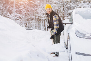 Man smiling while shoveling snow from driveway beside car, clearing winter blizzard after snowfall