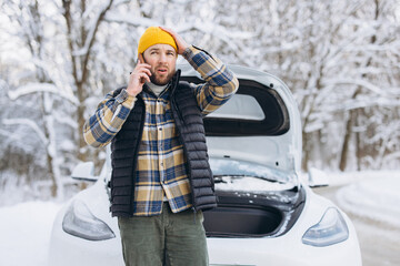 Man having car breakdown on snowy winter road, making emergency call for assistance with open hood