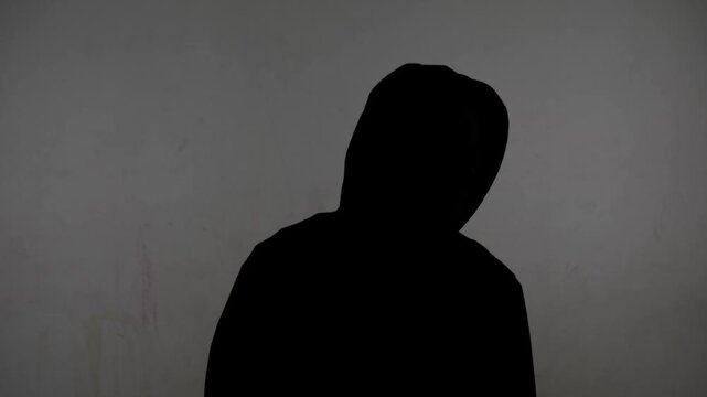 Anonymous person in dark clothing stands against a plain wall while sharing thoughts and feelings
