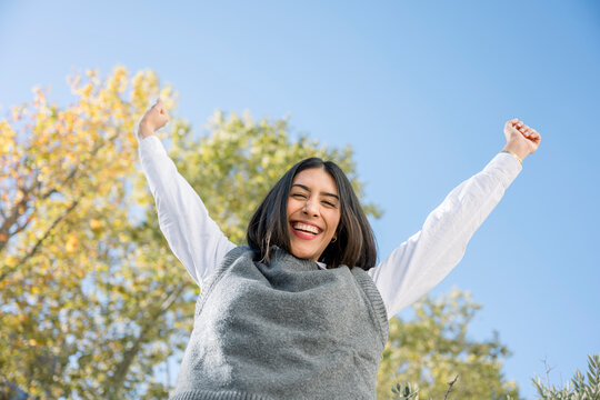 Young woman celebrating success with arms raised outdoors
