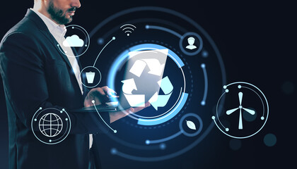 Businessman using laptop with digital recycling icons and eco conservation symbols on dark futuristic background illustrating green technology concept.