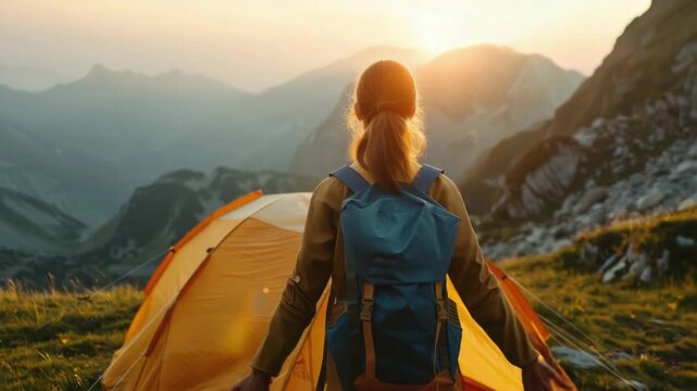 Exhilarated hiker in backpack and camping gear with arms wide open against a breathtaking sunrise backdrop of rugged mountain peaks