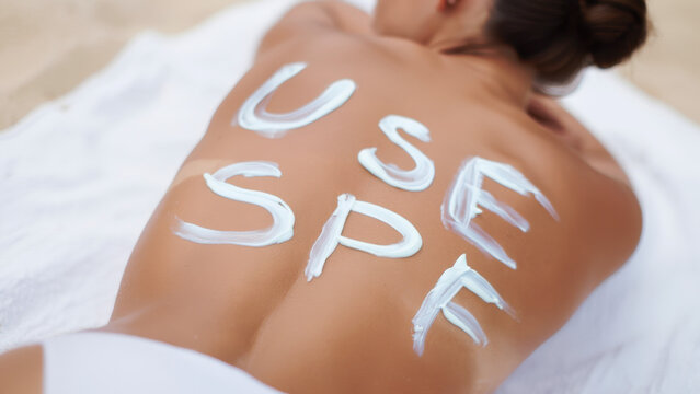 Sunscreen reminder written on skin with cream on a beach towel, promoting sun protection, skincare awareness during summer, UV ray defense message, outdoor health precaution concept - Powered by Adobe