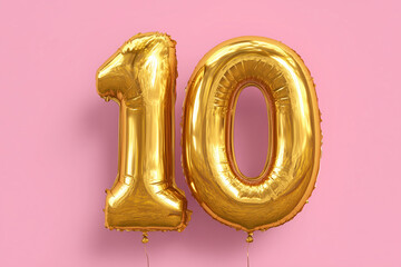Golden happy birthday foil balloon in shape of number 10 title inscription against pastel pink background. 
