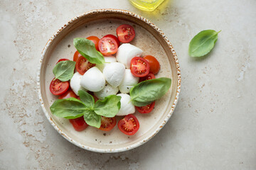 Italian caprese salad with bocconcini on a light-beige stone background, horizontal shot, above view