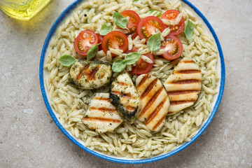 Plate of orzo with basil oil, cherry tomatoes and grilled halloumi cheese, horizontal shot, elevated view