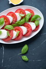 Classic caprese with sliced mozzarella, ripe tomatoes and fresh green basil, vertical shot on a black marble background, middle closeup