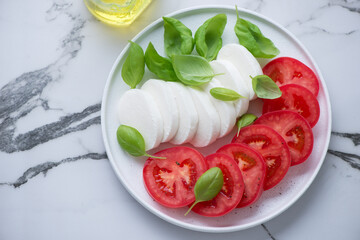 Plate with components for making italian classic caprese salad on a white marble background, horizontal shot, high angle view
