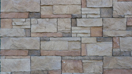 Obraz premium A fragment of a tiled wall made of natural stone, a mosaic of square shapes of different sizes in a gray-brown color scheme, decorative stone finishing tiles in the design of exterior surfaces