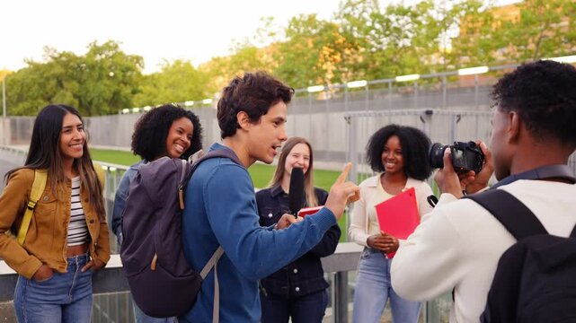 Group of young, diverse university students filming an interview on campus. Man speaks into a microphone while a friend records him