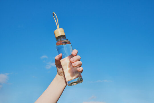 Hand holding reusable glass water bottle with water for hydration and sustainability