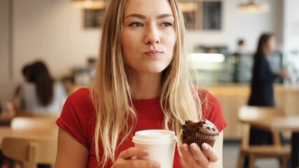 Young woman enjoys coffee and cupcake at cozy cafe. She smiles while savoring delicious dessert and warm drink. Relaxing atmosphere enhances joyful experience.
