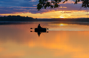 Man fishing on lake from small  boat at sunset. Fisherman silhouette at sunset. Summer time