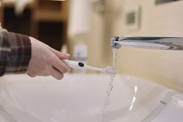 Toothbrush under running water in a bathroom sink, close up of routine hygiene and dental care as a...