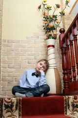 A bored little boy sits on the landing floor, leaning his head against a large floor vase.